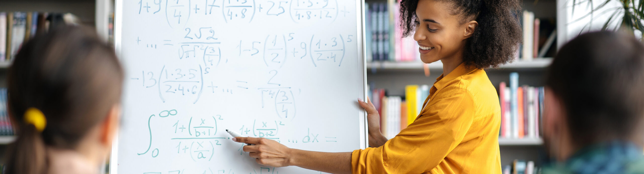 A Black female teaches students about math equations written on a whiteboard