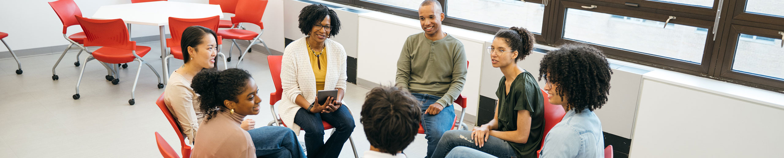 Group of young adults talking in a classroom and sitting in a circle.